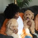 Woman sitting on a sofa with two brown pet poodle dogs.