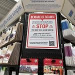 A large 'beware of scams' sign on display at a gift card aisle in a store.