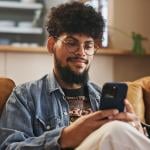 A young man smiling while typing on a smartphone.