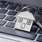 A house key and steel house keychain on top of a laptop keyboard.