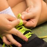 A young boy's hands tying shoelaces by himself.