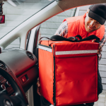 A food delivery person putting zipping up his delivery bag in his car.