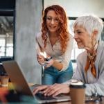 A senior employee working with a younger colleague on a task in an office.