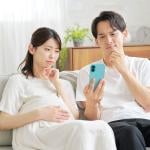 A pregnant wife and her husband curiously browsing information on a smartphone while sitting on a sofa at home.