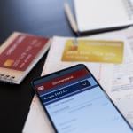 A close up on a credit card statement opened from a phone on top of physical credit cards and receipts.