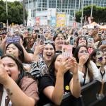 A crowd of fans holding their phones up and cheering outside the Crypto.com Arena for a K-Pop concert in Los Angeles, California.
