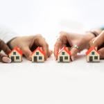 People's hand holding tiny models of houses.