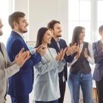 A business team standing and clapping together for a speaker.