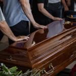 People touching the wooden brown coffin of a deceased relative.