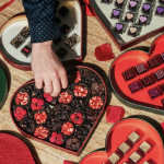 Person picking from a heart-shaped box of chocolates.