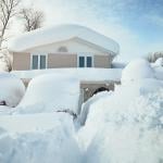 A house and its cars covered in deep white snow after a blizzard.