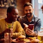 Happy men looking on their phones while sitting in a bar.