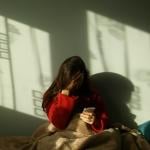 A sad woman in bed making a call on her phone.