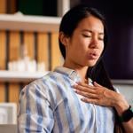 A young woman with her hand on her chest, practicing a breathing technique at home.