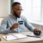 A black businessman using credit card to purchase online while in the office.