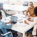Four members of a business team engaged in a project discussion around a table.