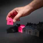 Figures of pink model houses being lined up with a row of black houses as a concept of national housing supply.