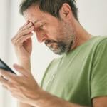 Man at home reading a worrying text message.
