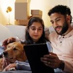 A couple with their dog relaxing in their new home and watching from a tablet.