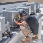 An HVAC tech at a rooftop checking a condenser unit.