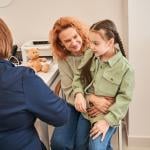 A little girl sitting on her parent's lap during a doctor's consultation.