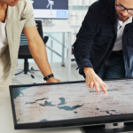 Two people looking at a U.S. map on a screen that is flat on a table in front of them.