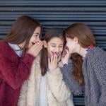 A group of three girls giggling and whispering with each other.