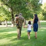 Back view of happy family walking together in a park. The father is wearing camouflage military uniform.