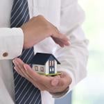A real estate agent holding a small figure of a house in a protective gesture as a concept of insurance.