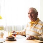 A happy senior old man seated by a dining table with cake.