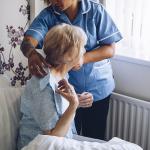 A home caregiver helping a senior woman get dressed in bed.