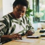 A black woman reviewing and calculating financial reports at home.