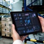 A business data dashboard in an iPad is shown and held by a marketing officer in a stock room.