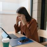 A woman employee who appears to be stressed sits in her workplace desk.