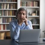 A pensive middle-aged woman thinking while sitting at a table in an office.