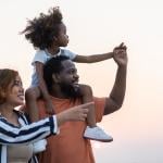 A portrait of a happy family with the daughter being carried by the father on his shoulders.