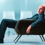 An elderly business person slouching in a chair at an office.