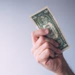 A focused photo of a person holding a one dollar bill.