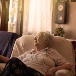 An old woman sitting on a sofa at home.
