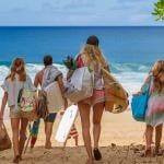 A family of four with their bags walking towards a white sand beach.