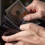 A person taking out dollar bills from a wallet.