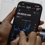 Person monitoring smartphone displaying Brent crude oil prices in USD.