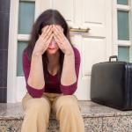Woman sitting by the entrance of a home in a disappointed gesture.