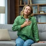 A woman sitting on a sofa holding her chest due to pain.