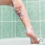 A close-up of a person shaving her leg in a bathroom. 