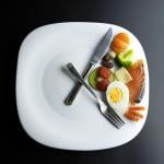 A plate of healthy ingredients simulating a clock with its hands represented by a knife and a fork as a concept of intermittent fasting.
