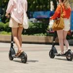 Two women riding electric scooters outdoors.
