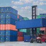 A forklift lifting a container van in a shipping yard.