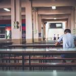 A male high school student sitting alone at a cafeteria.