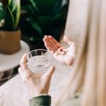 A woman holding multiple pills to drink with a glass of water.